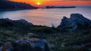 A sunset over a coastal landscape with rocky outcrops and calm water.