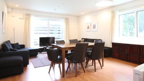 Ett modernt vardagsrum med ett matbord, stolar, en soffa, en TV och ett stort fönster med gardiner.