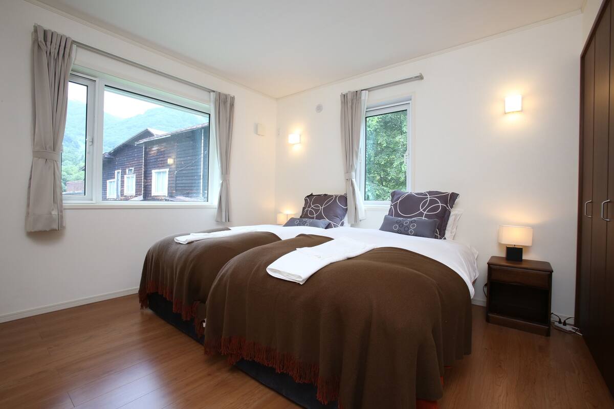 A double bed with two pillows, a bedside table with a lamp, and a window with curtains.