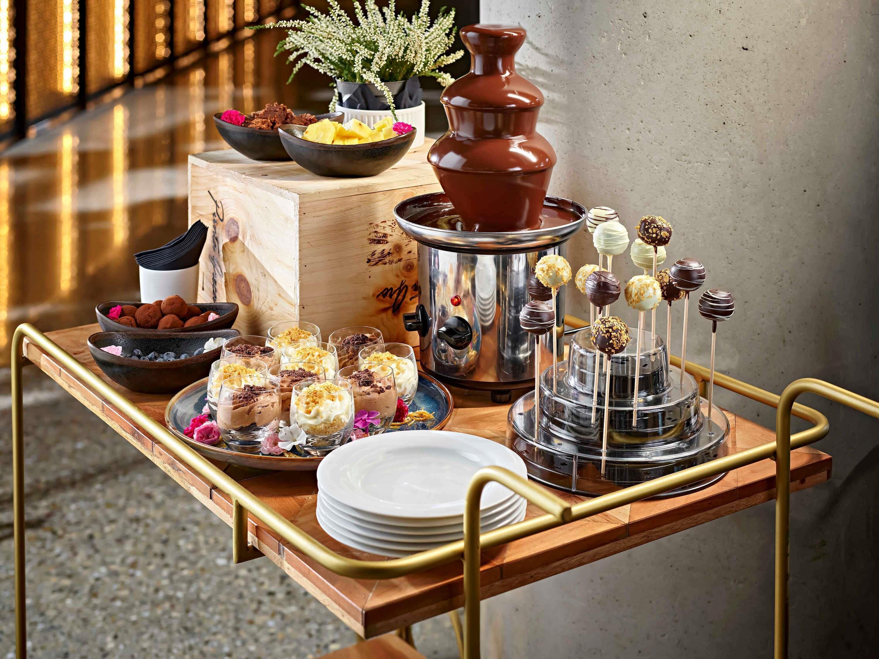 A wooden serving cart with various desserts, a coffee machine, and a potted plant.