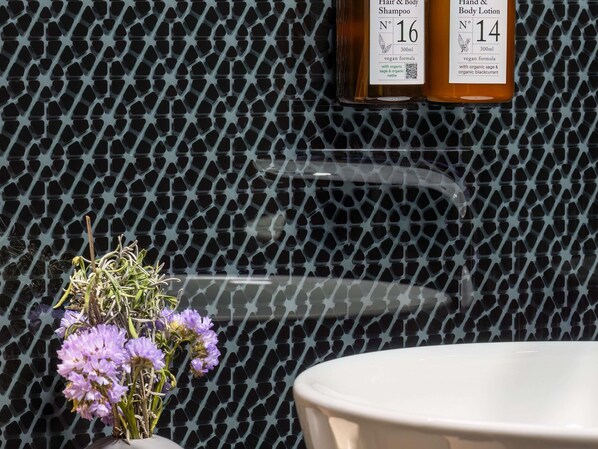 Un baño con pared de diseño, una bañera blanca y dos botellas de champú y loción.