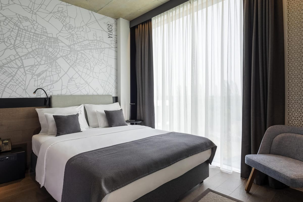 Een moderne hotelkamer met een groot bed, een stadsgezicht op de muur, een bureau met telefoon en een stoel.