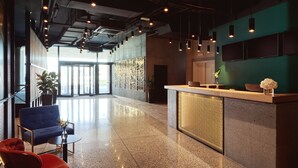 A modern reception area with a polished granite floor, a reception desk with a textured panel, and a blue armchair. - Mövenpick Zagreb (Zagreb)