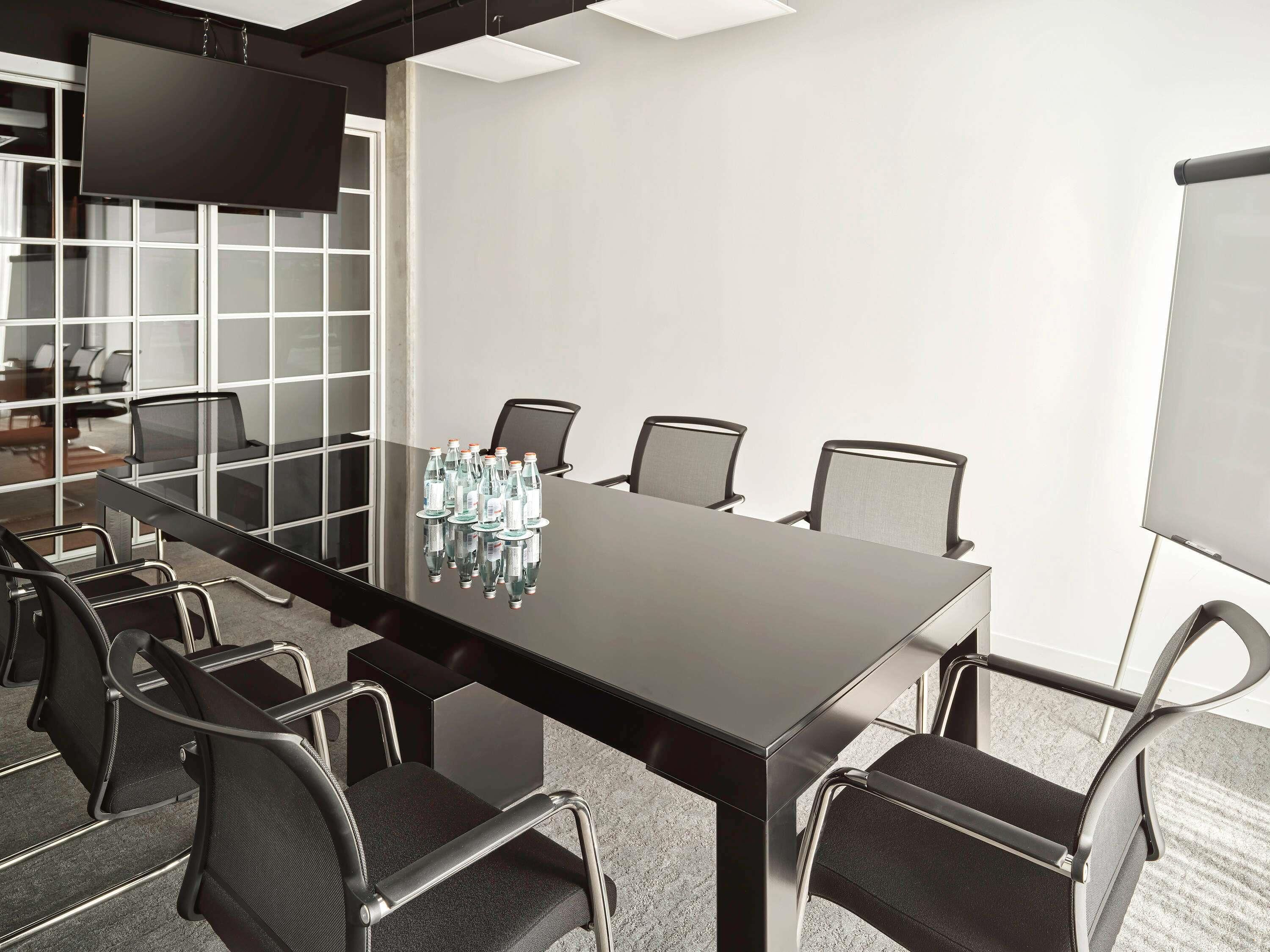 A conference room with a long table, six chairs, a flat-screen TV, and a whiteboard.