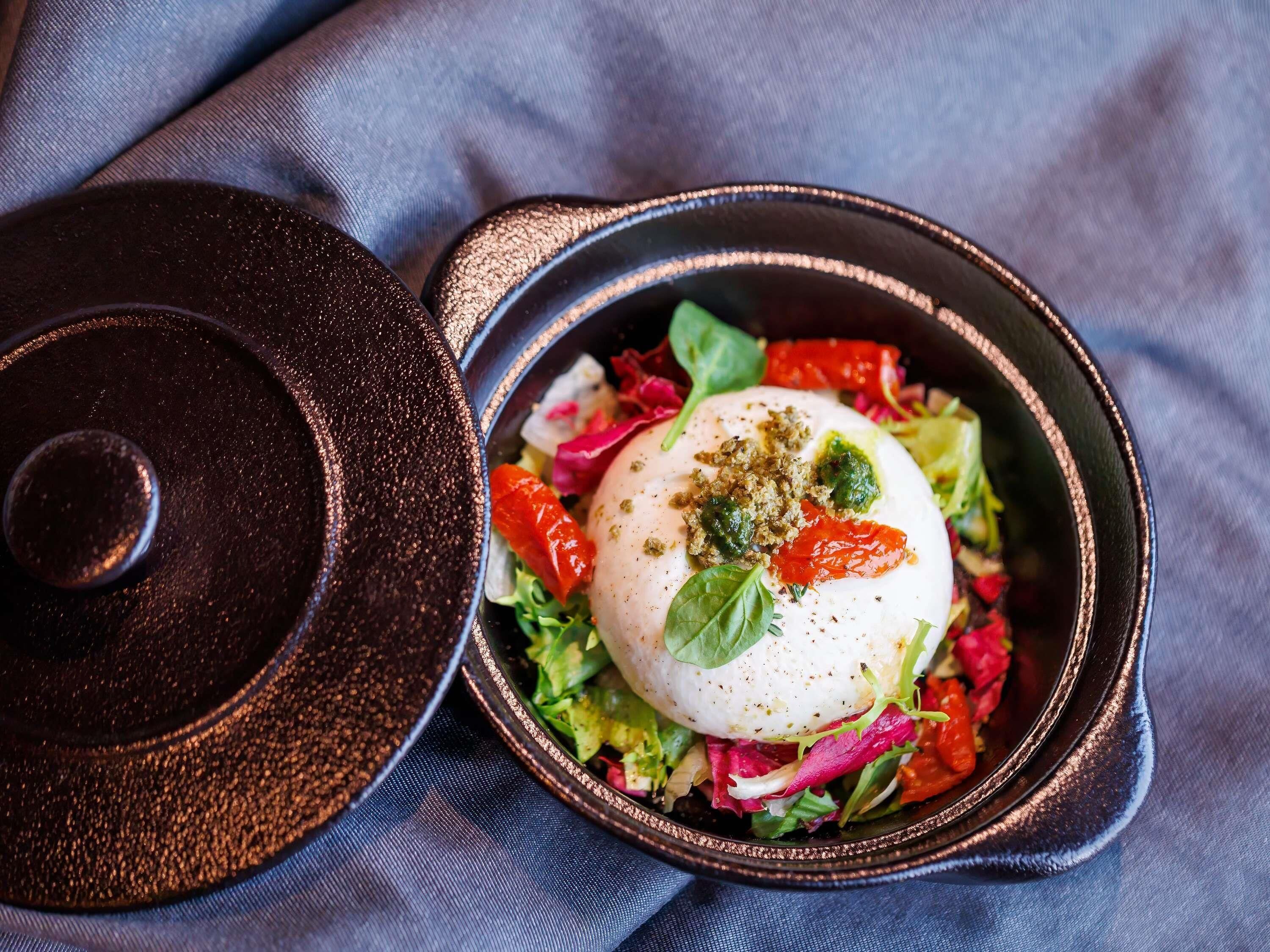 A bowl of salad with a poached egg, garnished with herbs and peppers, on a dark textured surface.