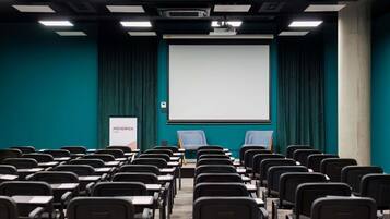 A conference room with rows of chairs, a large screen, and a projector.