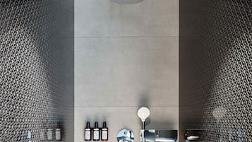 A modern shower area with a rain showerhead, handheld showerhead, and three bottles of shampoo.