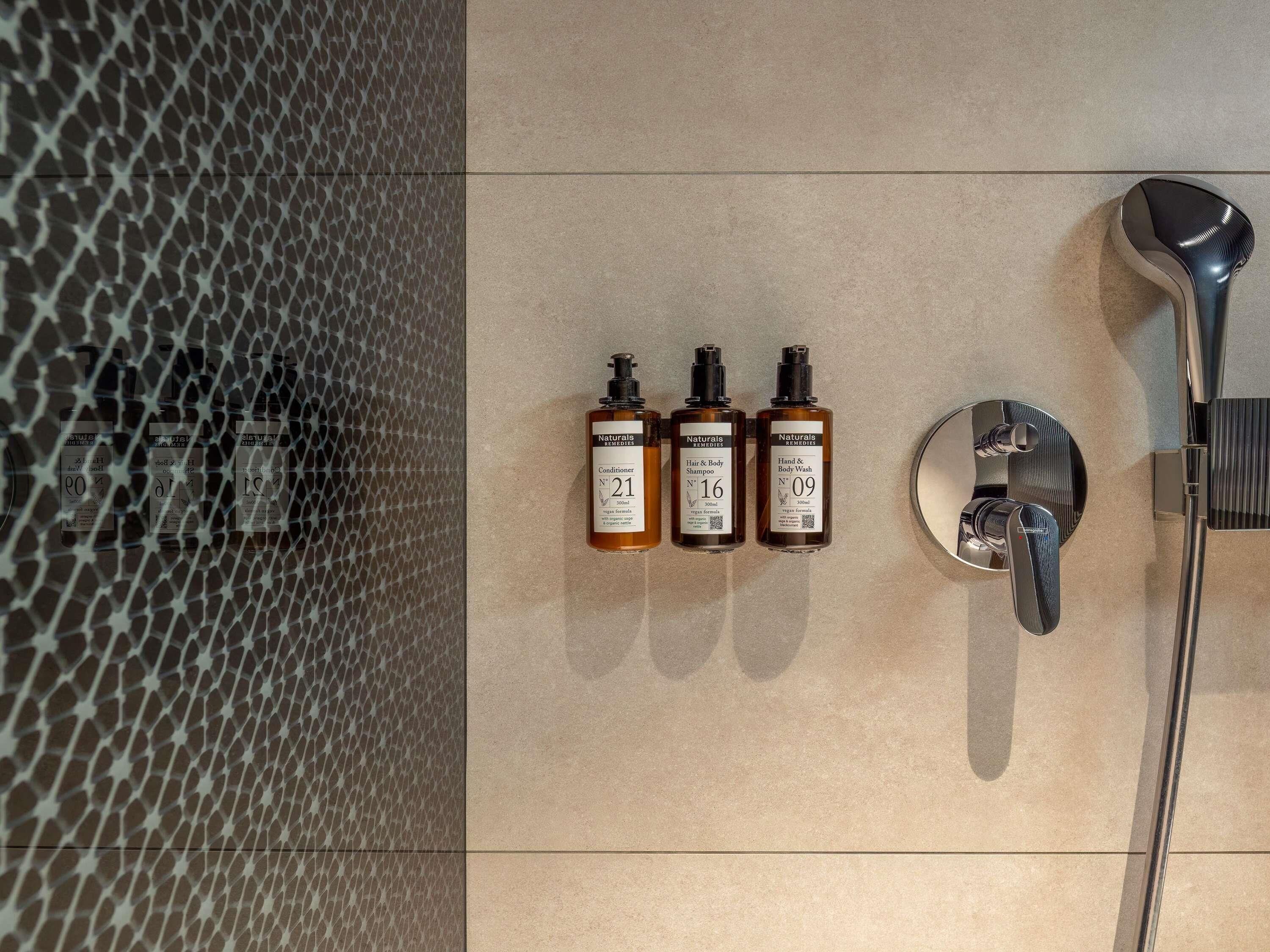 Un baño con ducha, tres botellas de productos capilares naturales y un espejo.