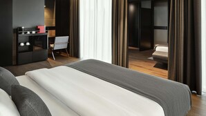 A modern hotel room with a large bed, a desk with a coffee machine, and a view through a curtain. - Mövenpick Zagreb (Zagreb)
