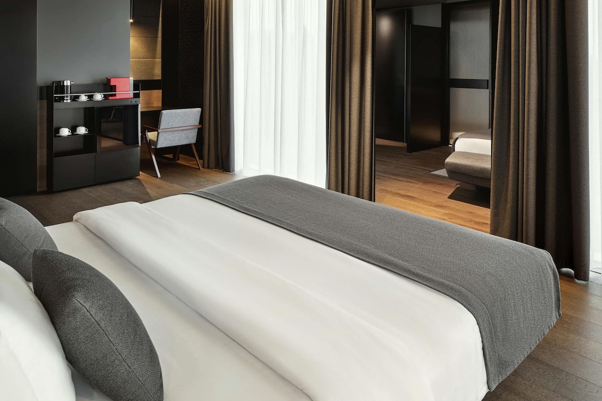Een moderne hotelkamer met een groot bed, een bureau met een koffiezetapparaat en uitzicht door een gordijn.