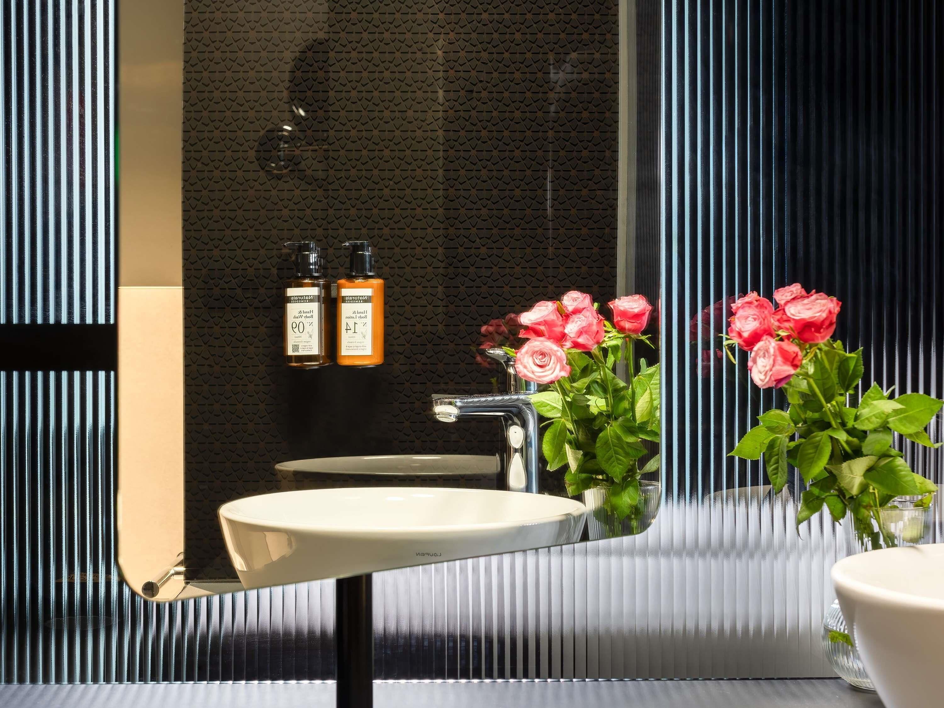 A bathroom with a large mirror, a sink, and two bottles of shampoo on a shelf.
