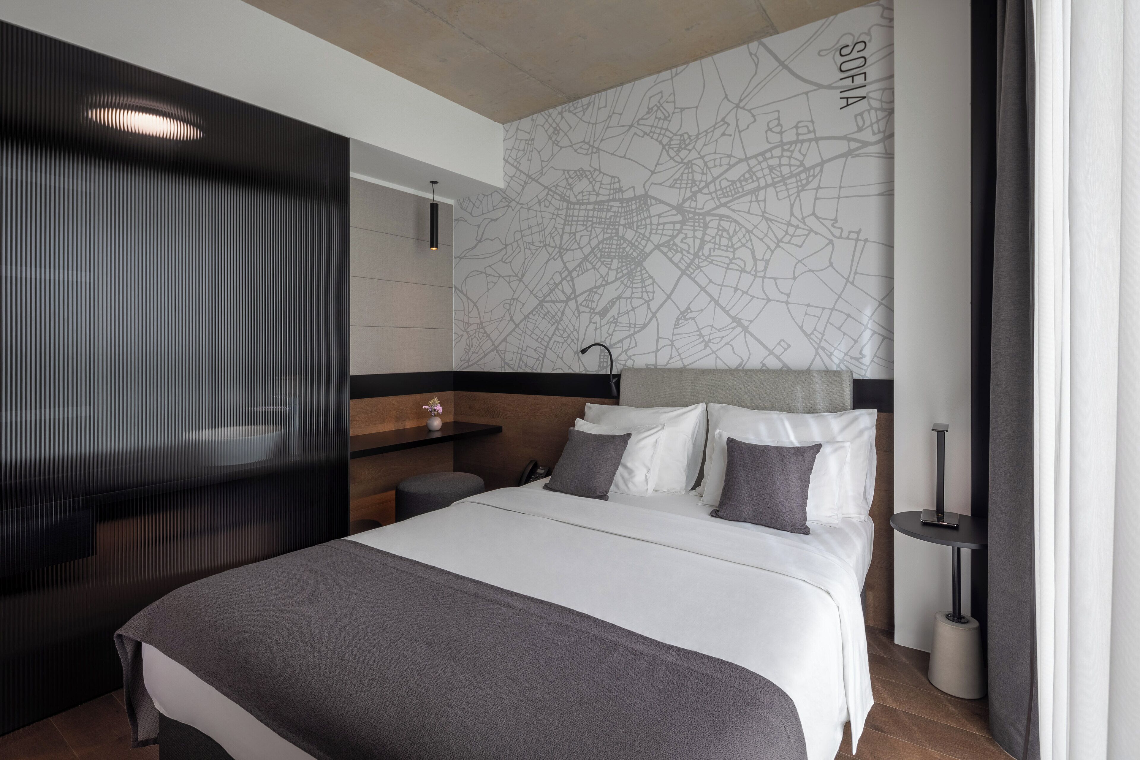 Une chambre d’hôtel moderne avec un grand lit, une carte accrochée au mur, un petit bureau et un miroir.