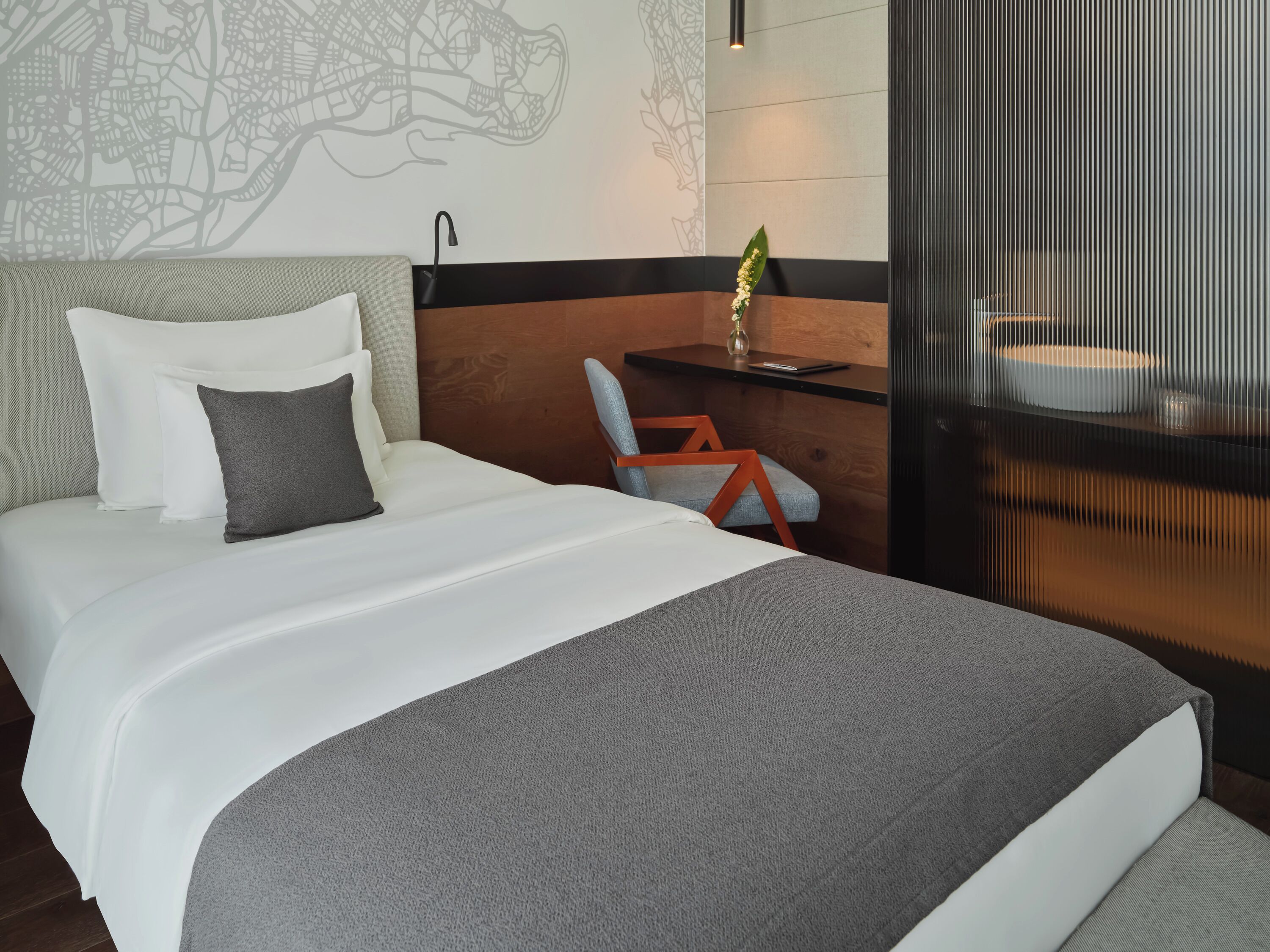 A modern hotel room with a neatly made bed, a desk with a chair, and a decorative wall.