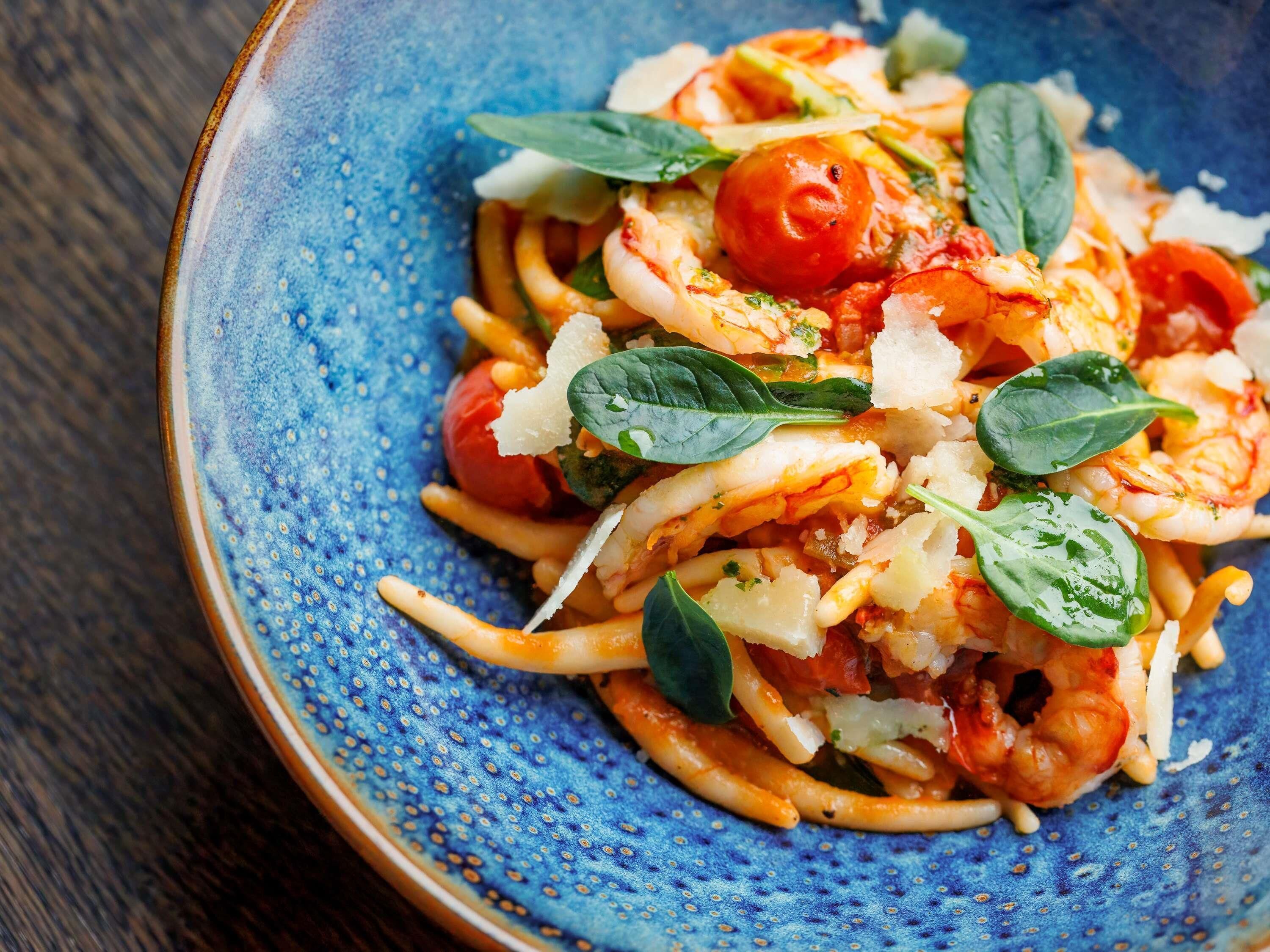 Une assiette de spaghettis aux crevettes, aux tomates cerises et aux feuilles de basilic.