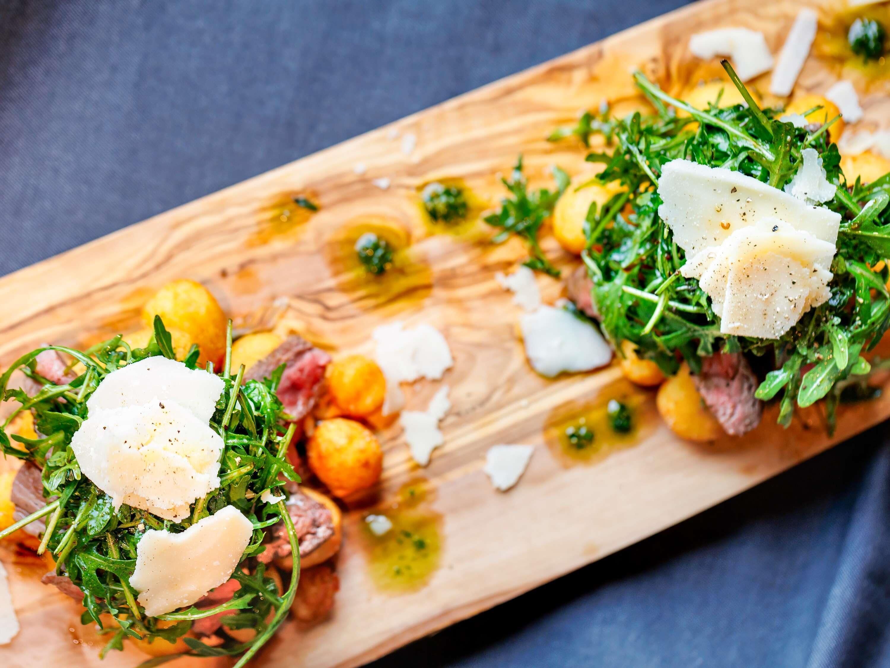 Una tabla de madera con ensalada de hojas verdes, queso y patatas asadas.