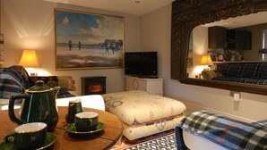 Een gezellige woonkamer met een televisie, een schilderij, een open haard en een eethoek met een gedekte tafel voor thee.