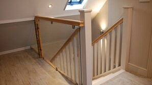 Een houten trap met een glazen balustrade, een dakraam en een lichtschakelaar op de muur.