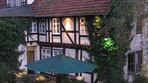 A traditional half-timbered house with a green umbrella and potted plants in the foreground. - Hotel Schlafschön (Hann. Muenden)