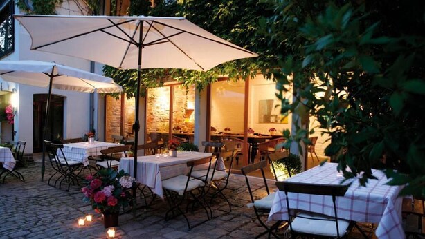 An outdoor dining area with tables and chairs, covered by umbrellas, and surrounded by greenery. - Hotel Schlafschön (Hann. Muenden)