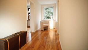 A hallway with wooden flooring, a white chair, and a window with a view of greenery. - Hotel Schlafschön (Hann. Muenden)