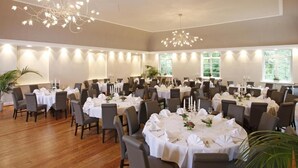 A large banquet hall with round tables set for a formal event, featuring chandeliers and natural light from large windows. - Hotel Schlafschön (Hann. Muenden)