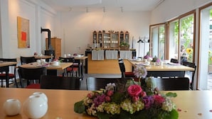 A restaurant with multiple tables and chairs, a wooden cabinet with glass doors, and a large window with a view of greenery. - Hotel Schlafschön (Hann. Muenden)
