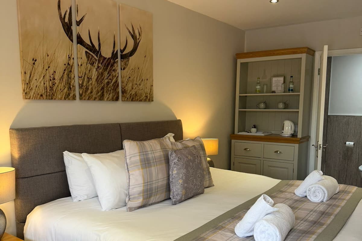 A neatly made bed with a plaid bedspread, a bedside table with a lamp, and a wall-mounted cabinet with toiletries.