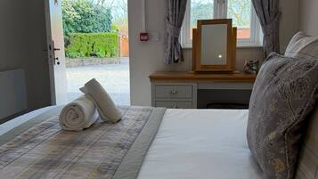 A hotel room with a bed, a bedside table with a mirror, a window with curtains, and a view of the outdoors.
