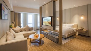 Une chambre d’hôtel moderne avec un canapé, une table basse ronde, un lit et un téléviseur fixé au mur.