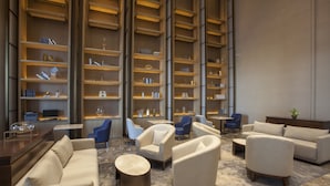Un hall d’hôtel moderne doté d’un espace salon central, d’un bar et d’une grande bibliothèque.