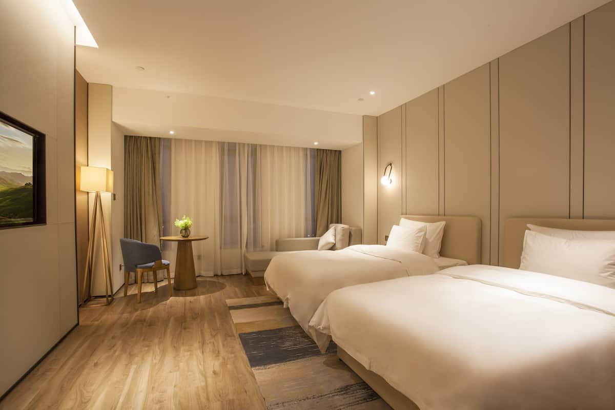 Une chambre d’hôtel avec deux lits, une petite table avec une lampe, une chaise et une vue sur un paysage par la fenêtre.