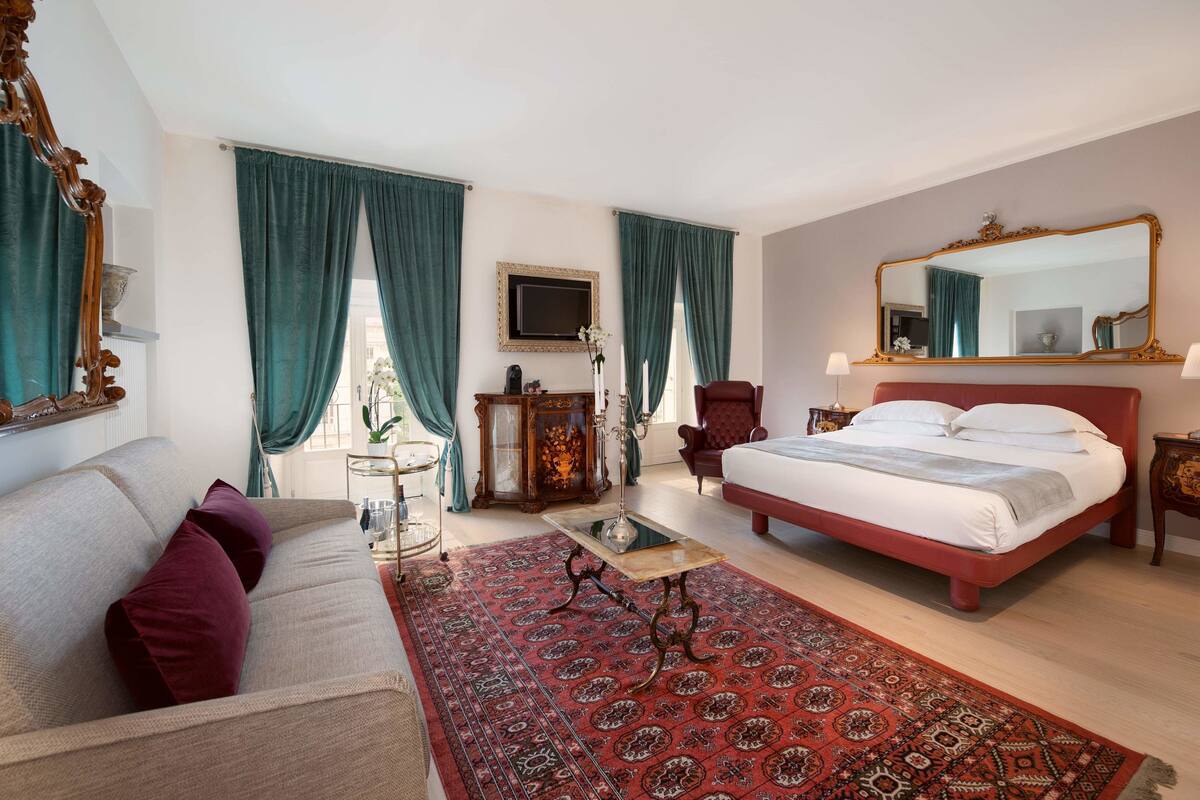 A bedroom with a bed, a sofa, a coffee table, a mirror, and a dresser.