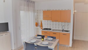 Een kleine keuken met moderne apparaten, een eethoek met een tafel gedekt voor twee personen, en een televisie op een kast.