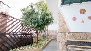 A courtyard with a stone wall, a metal fence, a small tree, and a bench.