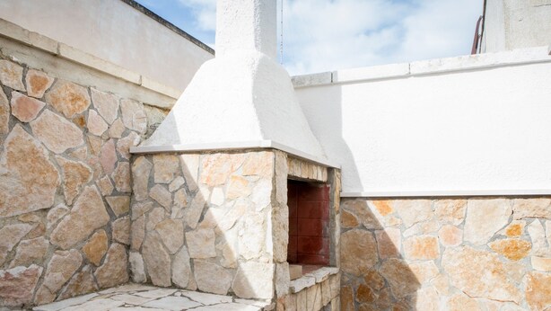 A stone-built outdoor oven with a white chimney, set against a white wall and stone base.