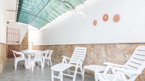 A sunlit patio area with white plastic chairs and a table, stone walls, and a metal gate.