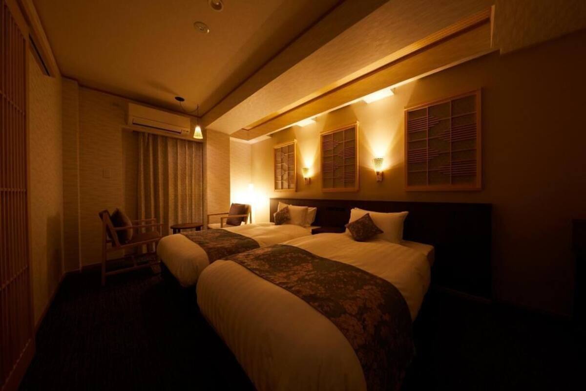 Ein Hotelzimmer mit zwei Betten, einem Sessel und Wandleuchten.