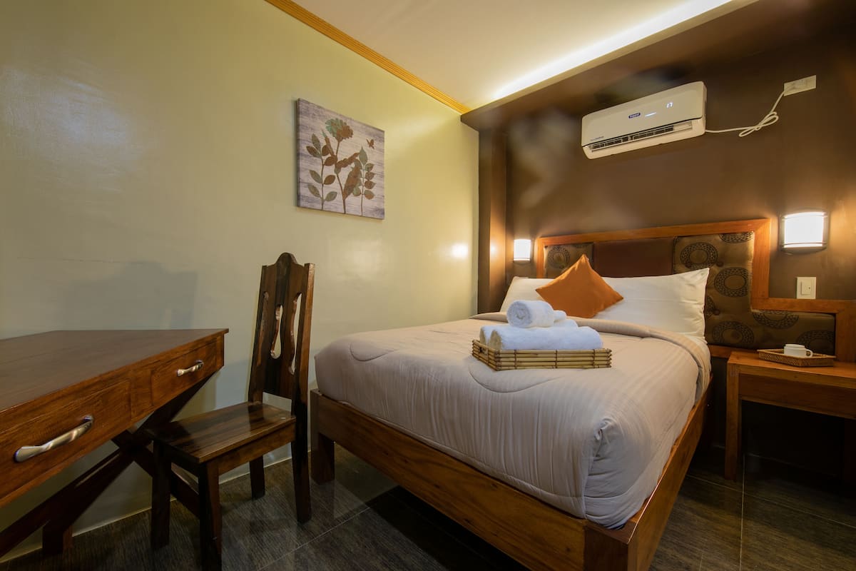 Une chambre d’hôtel bien rangée, avec un lit en bois, un bureau et une chaise.