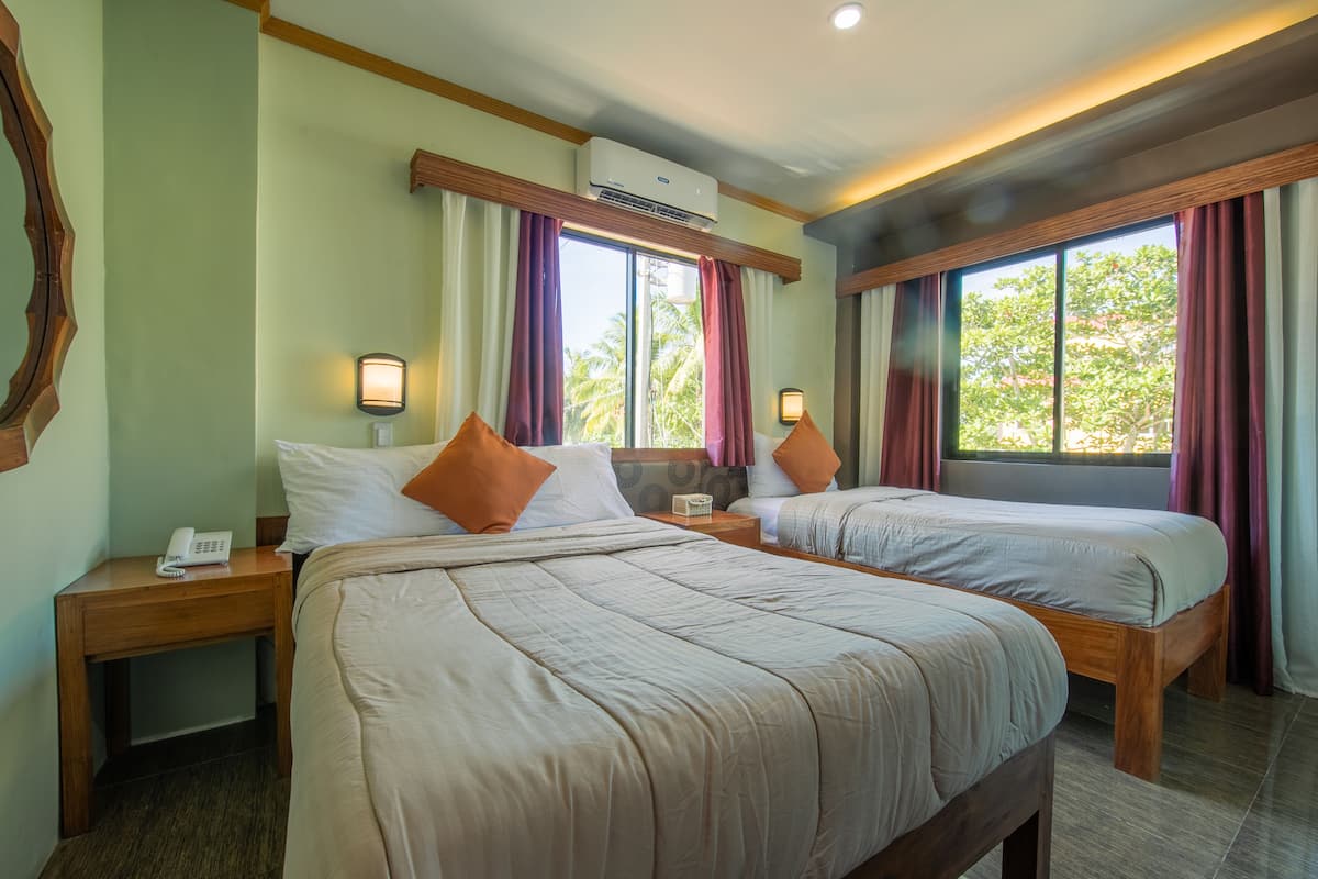 Une chambre d’hôtel avec deux lits, des têtes de lit en bois, une table de chevet avec un téléphone et un appareil de climatisation placé au-dessus de la fenêtre.