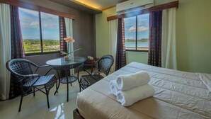Une chambre d’hôtel avec un lit, deux chaises, une petite table et une vue sur la mer.