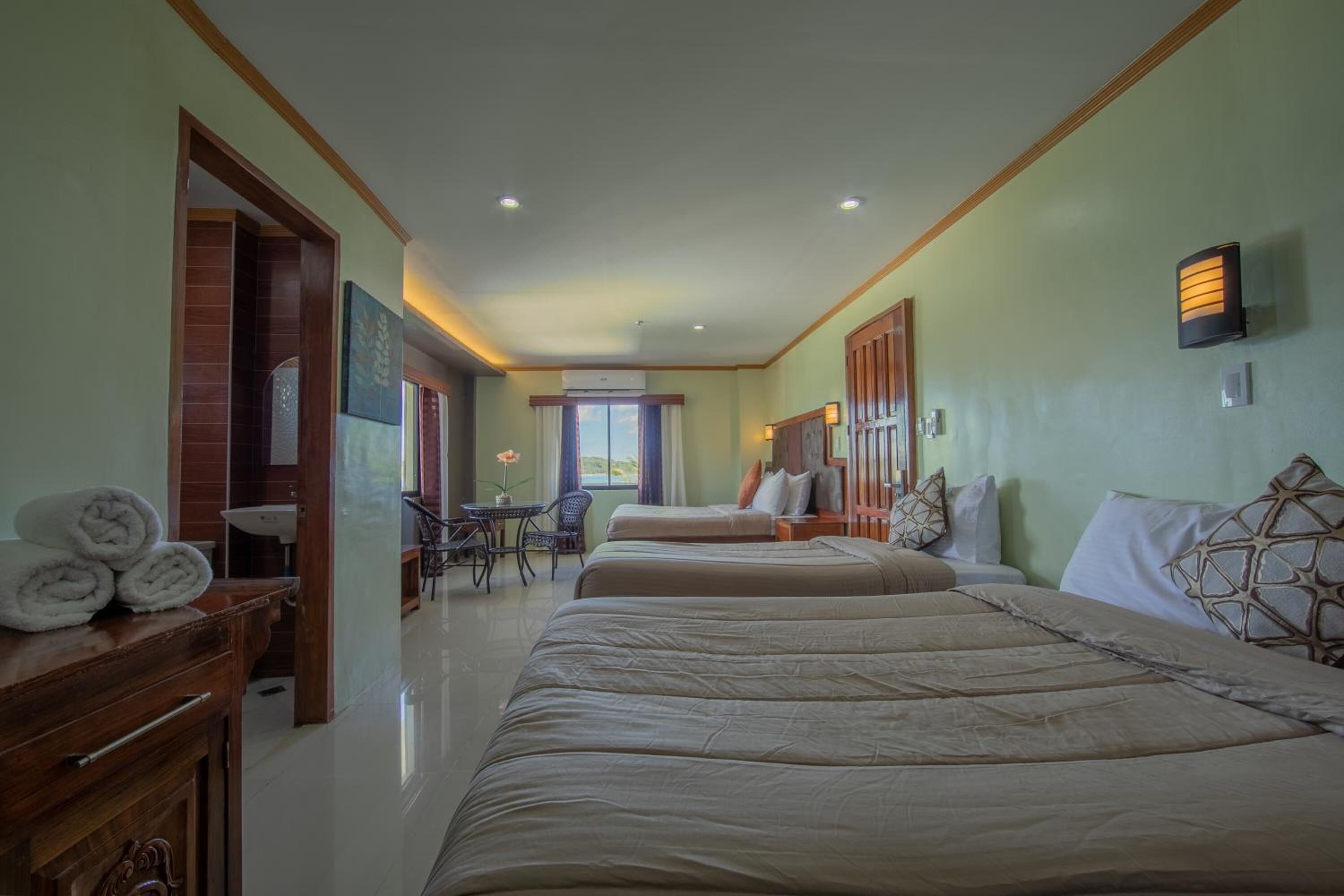 Une chambre d’hôtel avec deux lits, une commode en bois, une petite table avec une chaise et une fenêtre avec des rideaux.