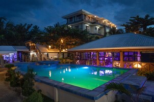 Una piscina con un deck circundante, un área de bar con asientos y un edificio de varios pisos y balcones.