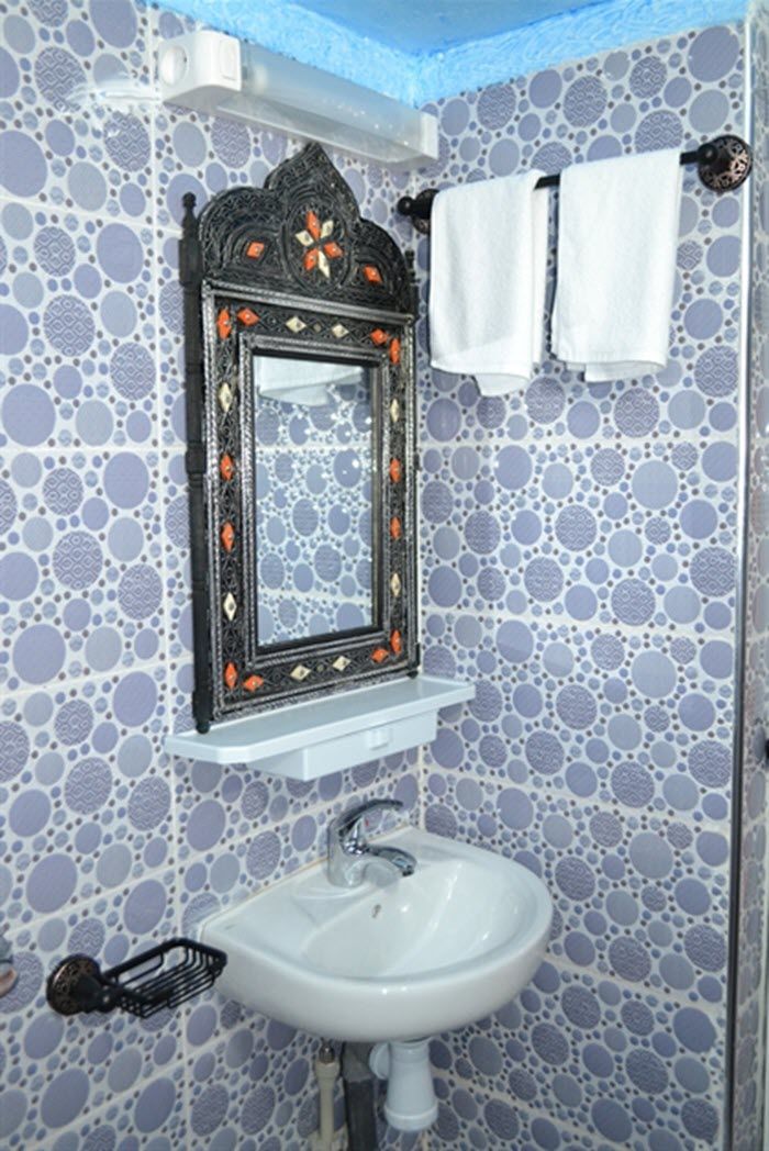 Un baño con un lavamanos blanco, un espejo decorativo y azulejos con diseños.
