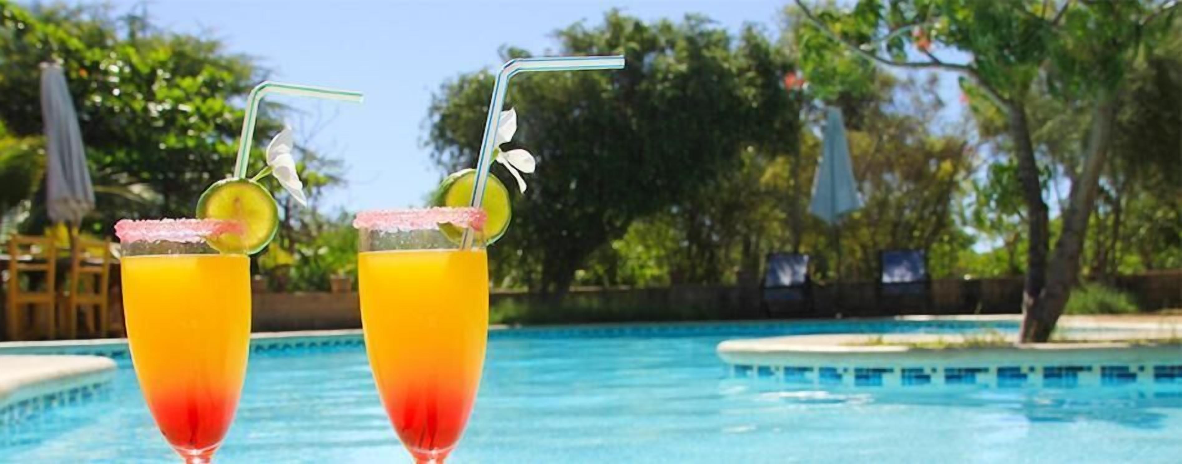 Dos cócteles con pajitas y rodajas de lima, frente a una piscina.