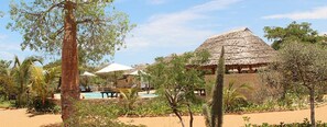 Een resort met een zwembad, gebouwen met rieten daken en palmbomen.