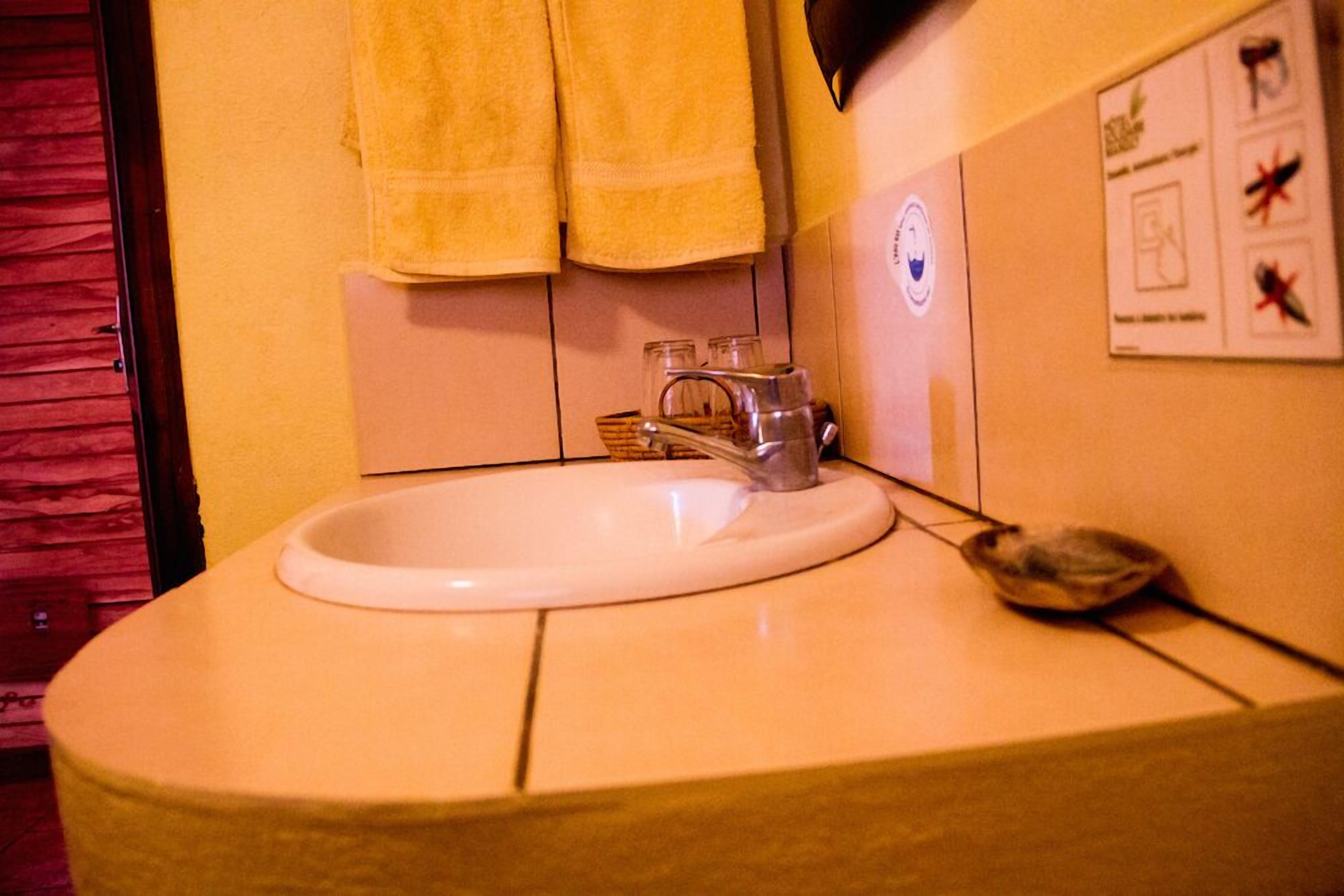 Un baño con un lavabo, dos toallas amarillas, un grifo y un dispensador de jabón en la pared.