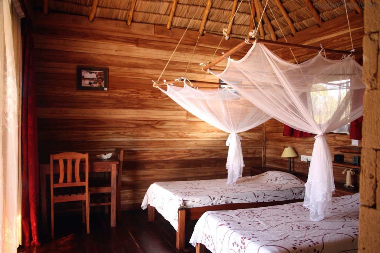 Una habitación de madera con dos camas, cada una con dosel. Hay una silla y una mesita.