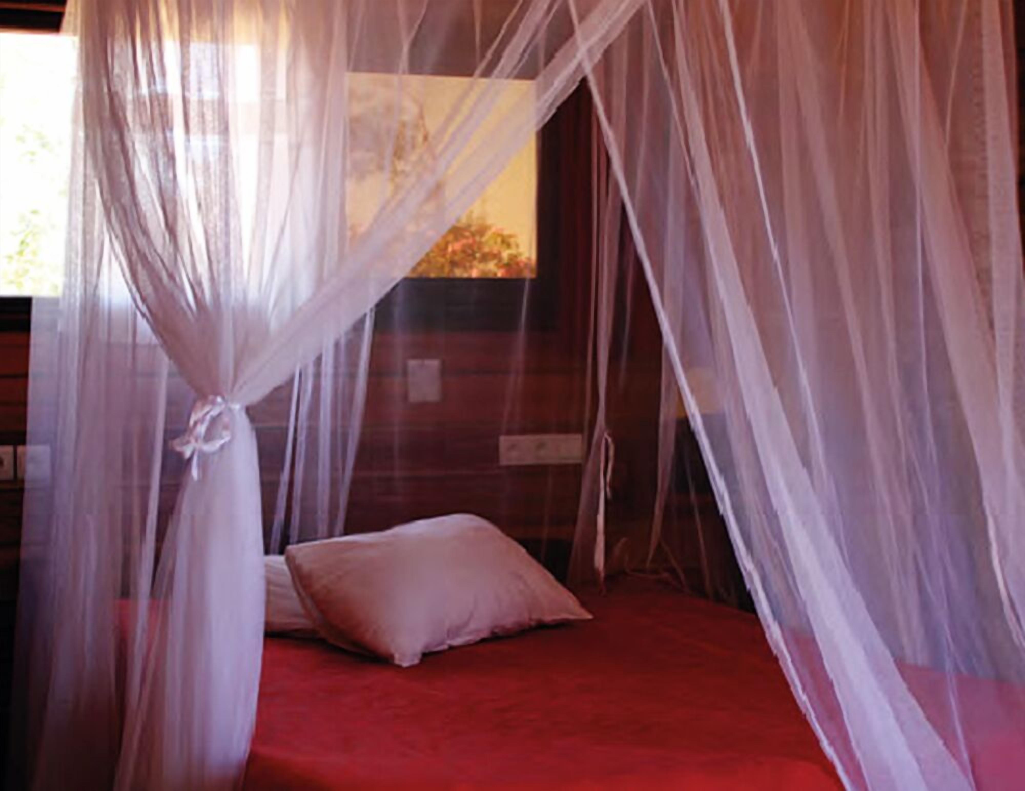 Una cama con colcha roja y almohada blanca, rodeada por un dosel blanco.