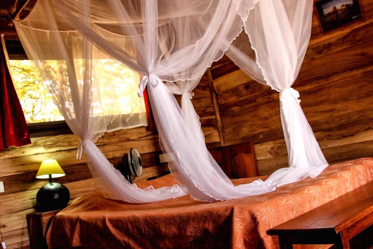 Habitación de cabaña de madera con una cama bajo un dosel blanco.