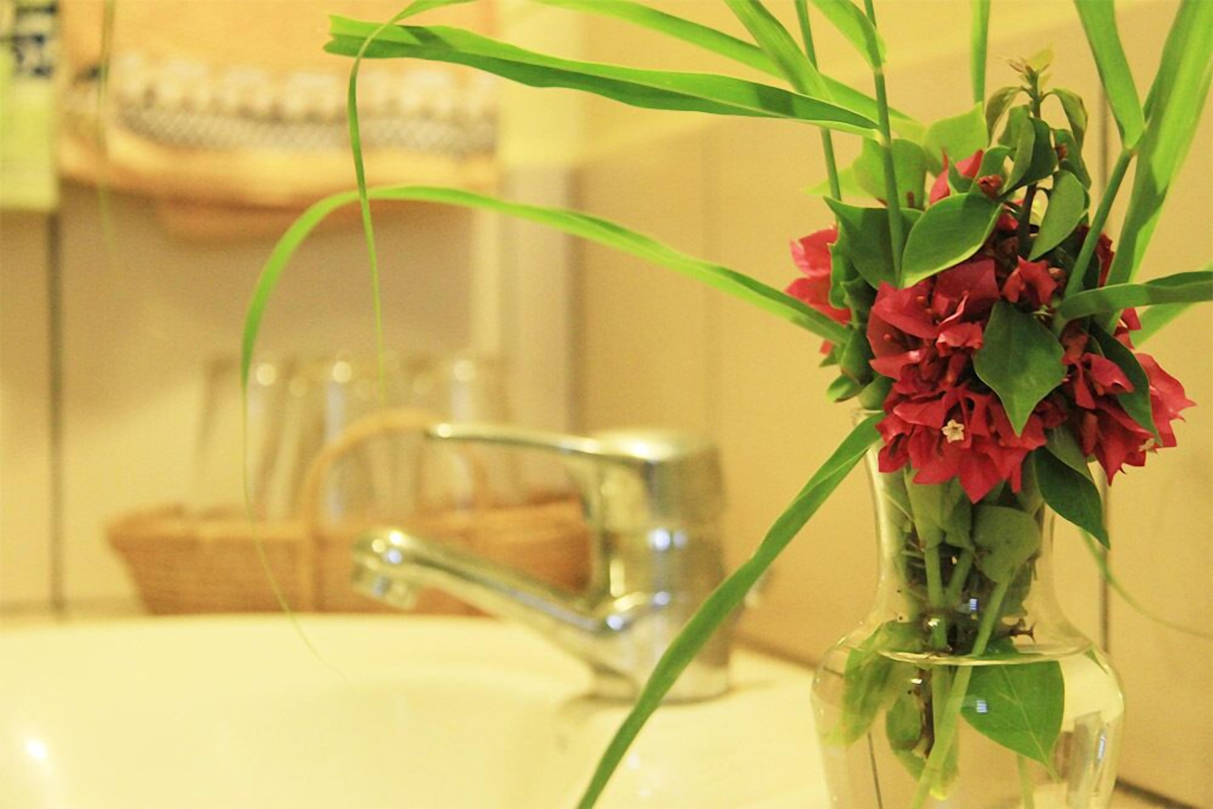 Un lavabo de salle de bain avec un vase transparent contenant des fleurs rouges et des feuilles vertes.